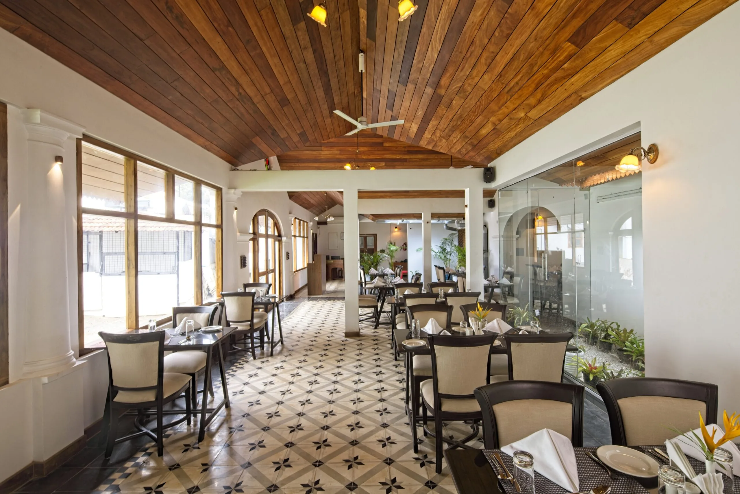 Dining tables beside the courtyard, framed by white columns and teak screens.