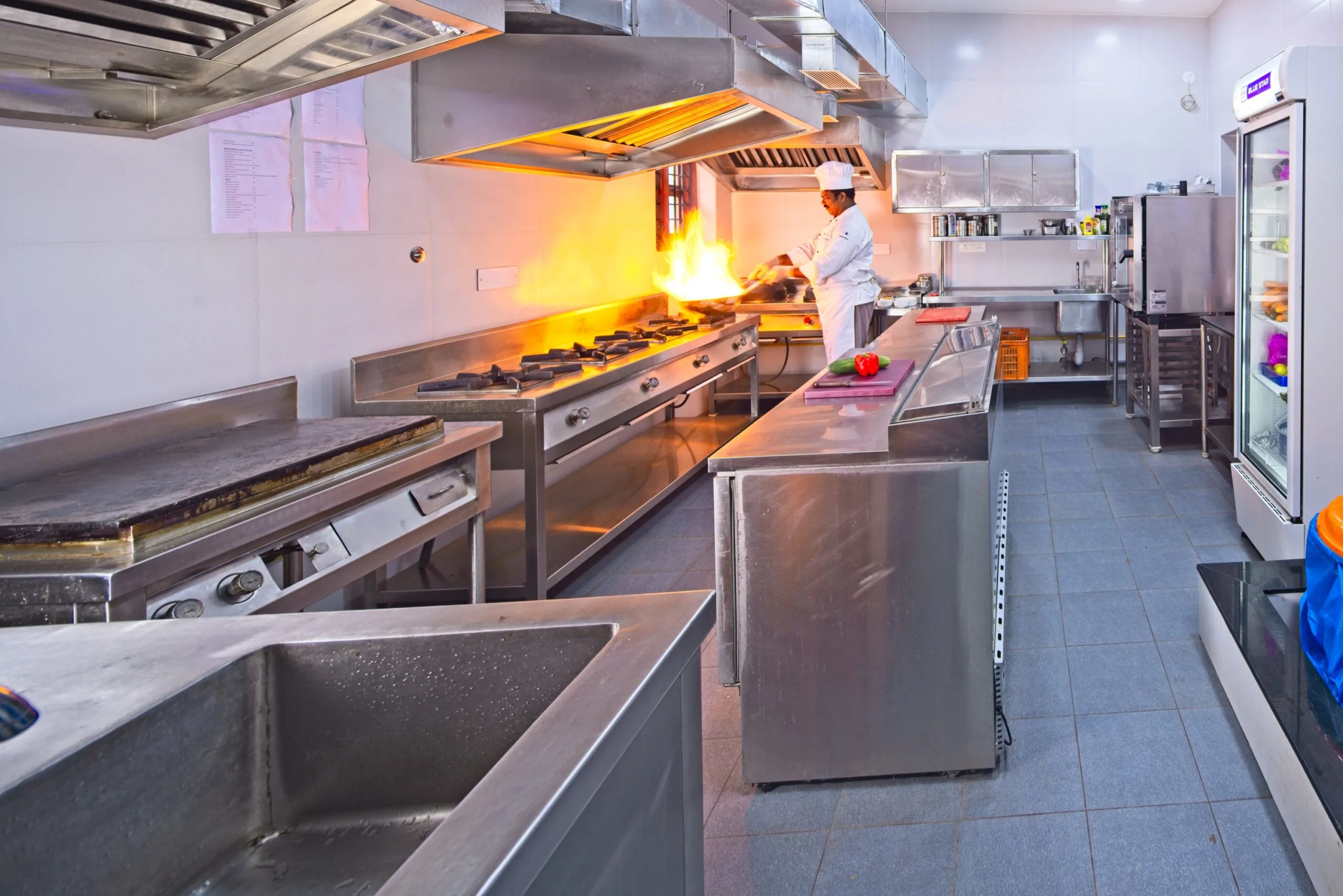 A chef in whites tossing a pan over an open flame in the restaurant kitchen.