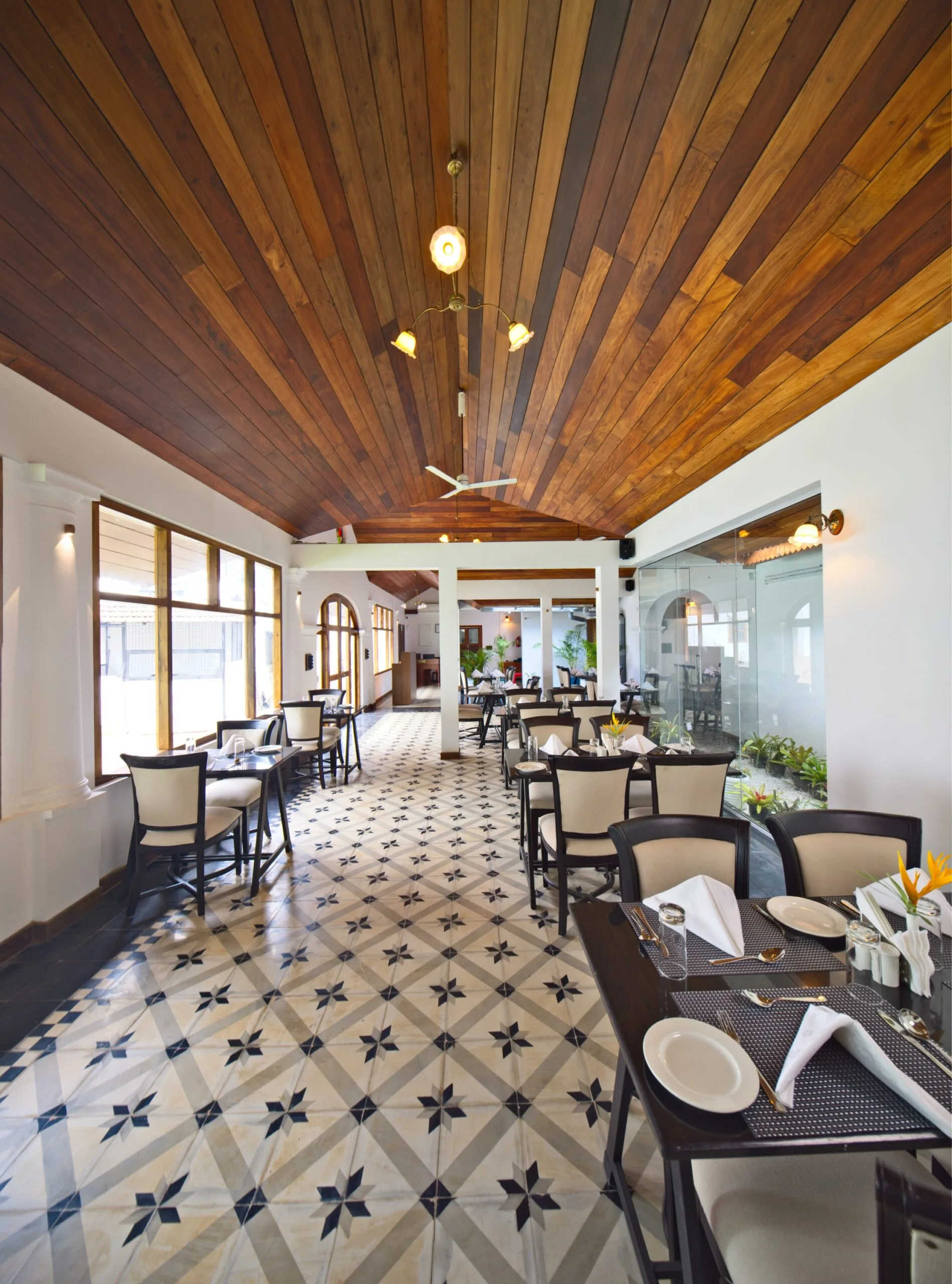 The long dining room lit by tall windows, teak ceiling above patterned tile.